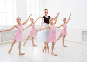 Young ballet teacher and students ballerinas in dance class. Girls are engaged in choreography in the ballet school.